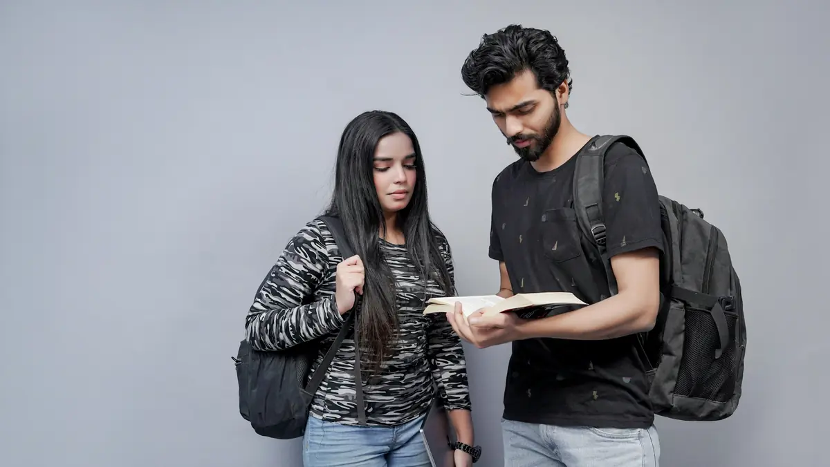 Two students with backpacks reading a book together